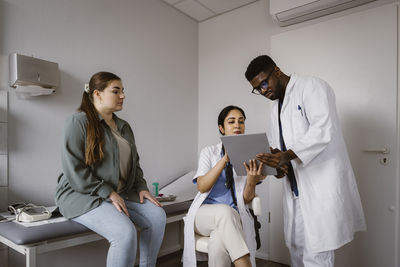 Male and female healthcare workers discussing over tablet pc with female patient in clinic