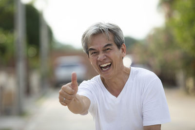 Portrait of mature man gesturing thumbs up while standing on street