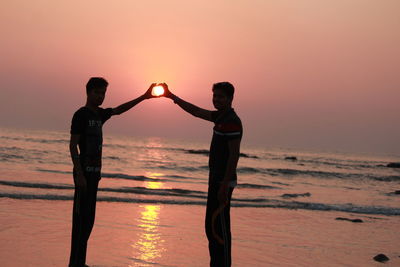 Full length of man standing on beach against sky during sunset