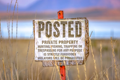 Close-up of information sign on field against sky