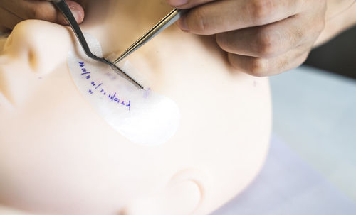 High angle view of hand sticking artificial eyelashes on mannequin