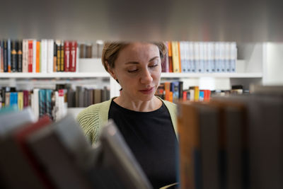 Scandinavian middle-aged woman choosing textbook, looking for literature while preparing for exam