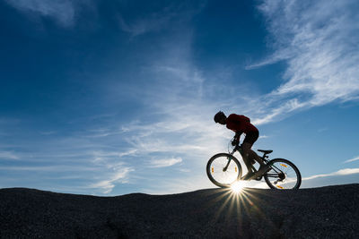 Silhouette man riding bicycle against sky