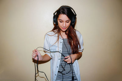 Woman wearing headphones while standing by wall