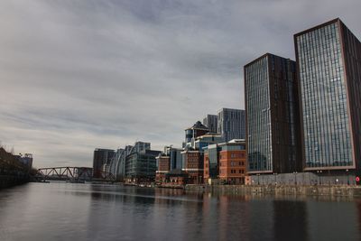 Modern buildings by river against sky in city