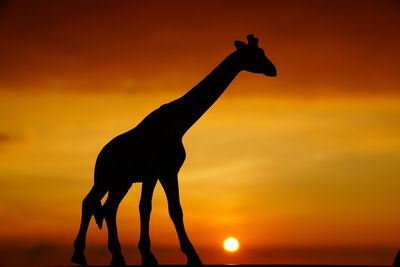 Close-up of silhouette giraffe toy against orange sky