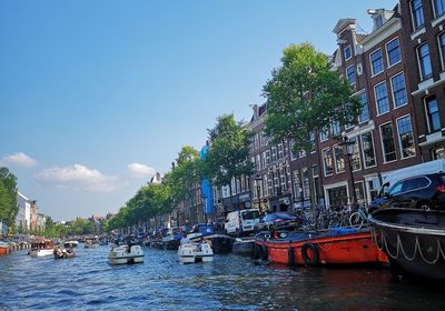 Sailboats moored in canal by buildings against sky