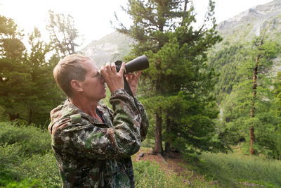 Side view of man looking through binoculars in forest