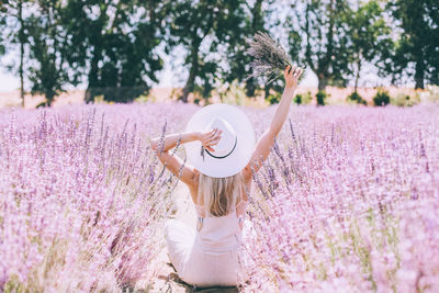 Rear view of woman wearing hat sitting amidst pink flowers in park