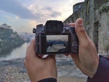 Cropped hands of man photographing river with camera during sunset