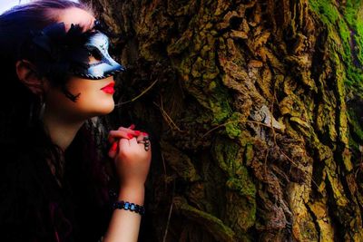 Close-up of woman wearing venetian mask while leaning on tree