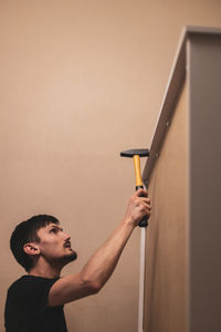 A young man hammers rivets into a closet with a hammer.