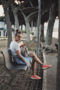 Side view of young woman sitting on bench