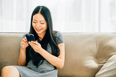 Young woman using phone while sitting on sofa at home