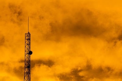 Low angle view of communications tower against orange sky