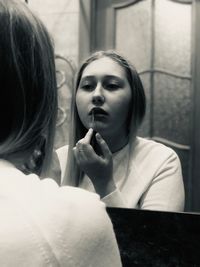 Reflection of woman applying lipstick in mirror at home