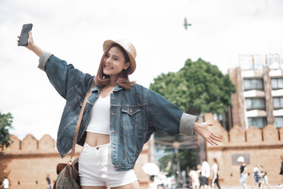 Young woman photographing with mobile phone standing outdoors