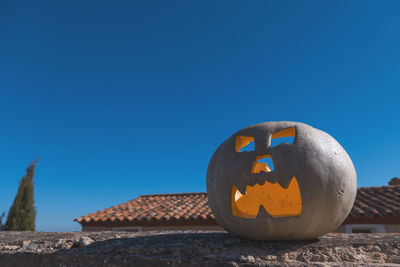 Low angle view of jack o lantern on retaining wall against clear blue sky