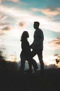 Silhouette couple standing on land against sky during sunset
