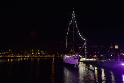 Sailboats in river against illuminated city at night