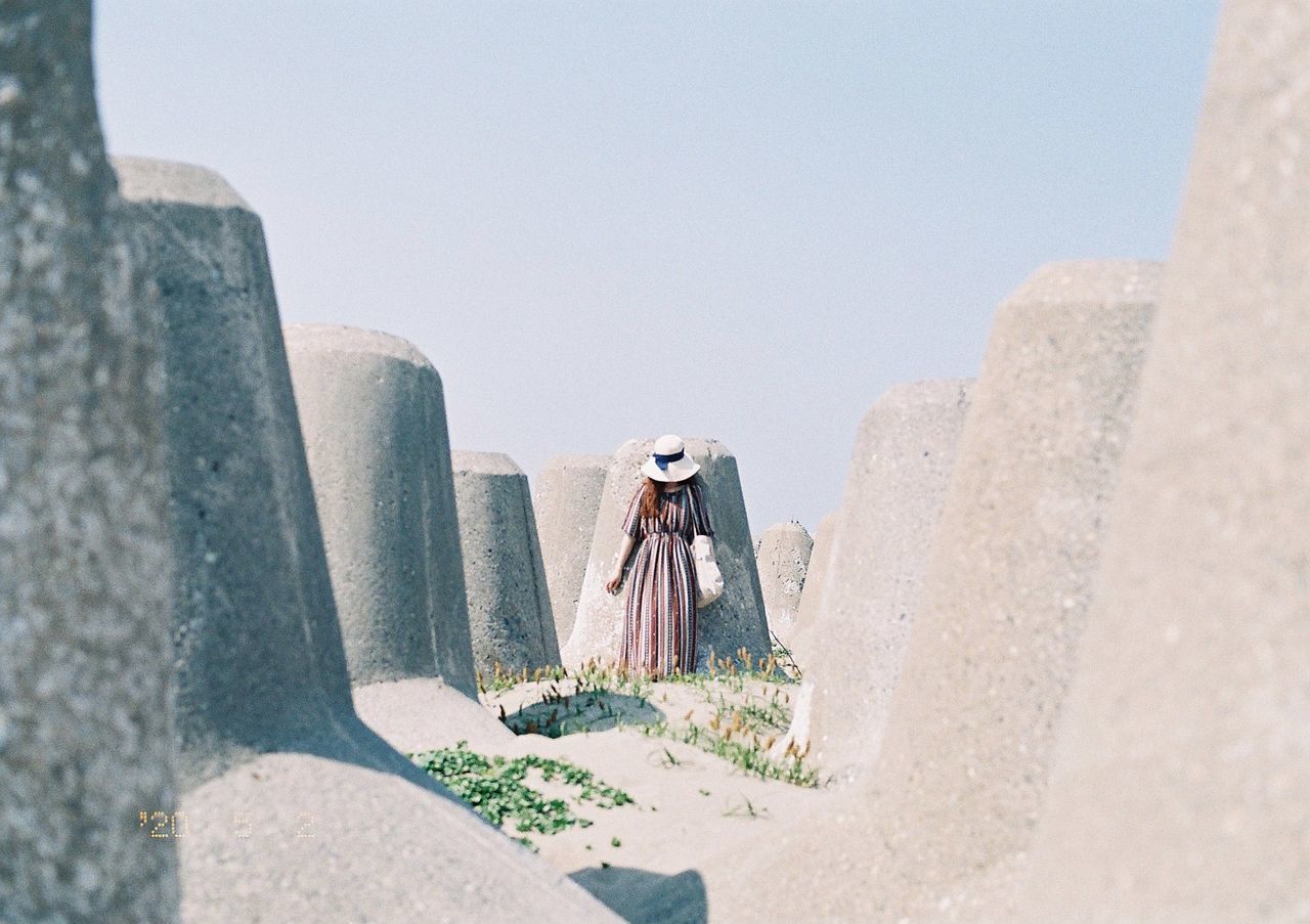 MAN LEANING ON ROCK AGAINST WALL AGAINST CLEAR SKY