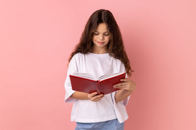 Portrait of young woman holding gift against pink background