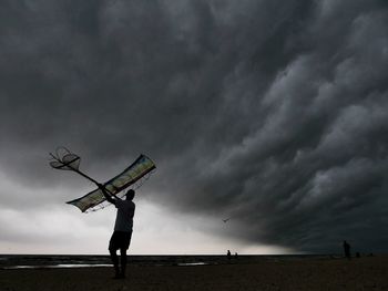 Silhouette man flying kite against storm clouds