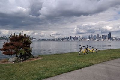 Bicycle by river in city against sky