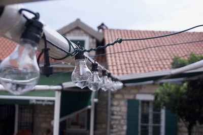 Light bulbs hanging on metal against house and sky