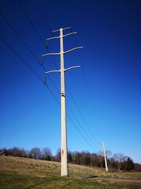 Low angle view of electricity pylon on field against clear blue sky