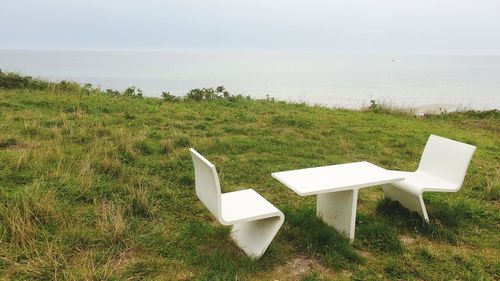 Deck chairs on field by sea against sky