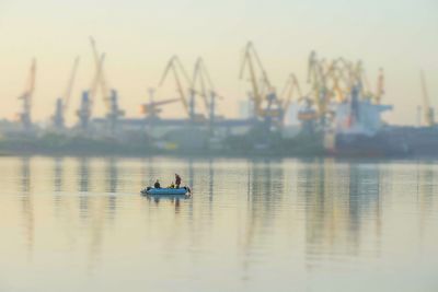 People sailing on boat by commercial dock against sky during sunset