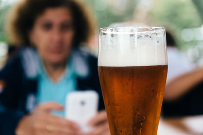 Close-up of beer glass with woman sitting in background