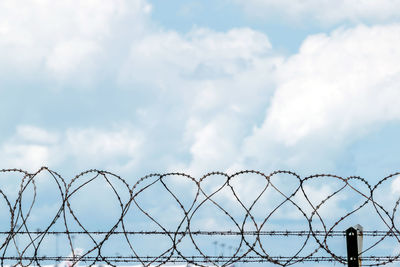 Closeup fence barbed wire with clouds sky background.