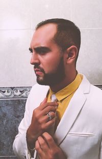 Businessman adjusting necktie against wall