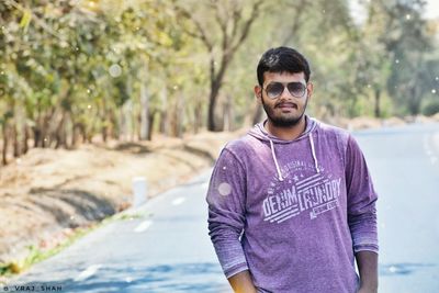 Portrait of young man wearing sunglasses standing against trees