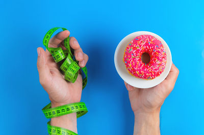 Cropped hands of woman holding donut against blue background