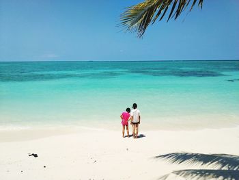 Rear view of sisters standing at beach against blue sky