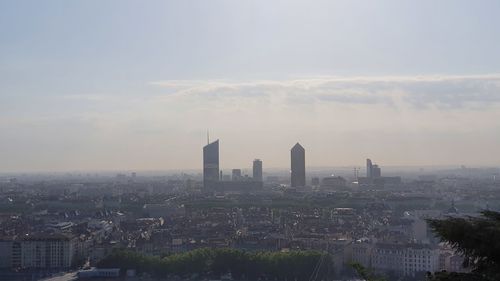 Aerial view of buildings in city against cloudy sky