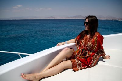 Young woman sitting in boat by sea against sky