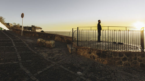 Side view of man looking at sea against sky during sunset