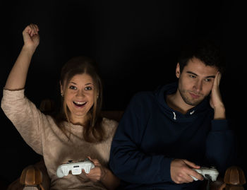 Portrait of woman with man playing video game against black background