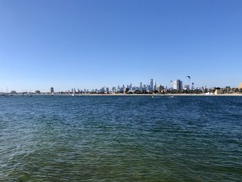 Sea by buildings against clear blue sky