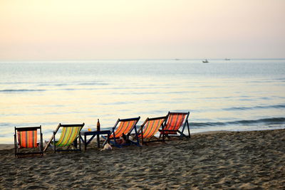 Chairs on beach against sky during sunset