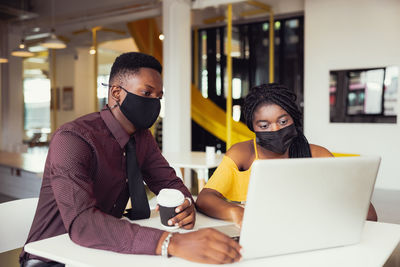 African students with friends wearing mask sitting at desk at modern school . virus protection