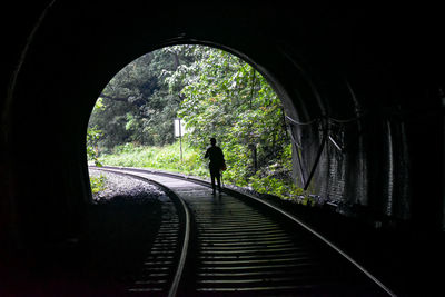Rear view of silhouette man on railroad tracks in tunnel