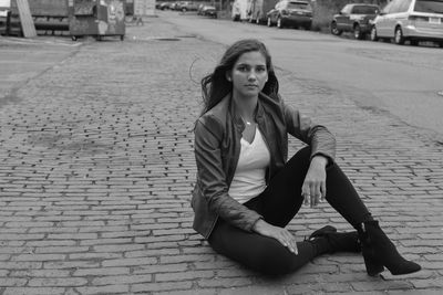 Portrait of young woman sitting on footpath in city