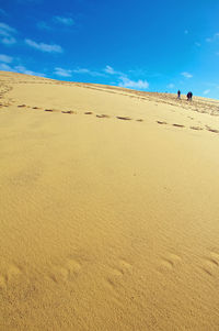 Sand dune on beach against blue sky