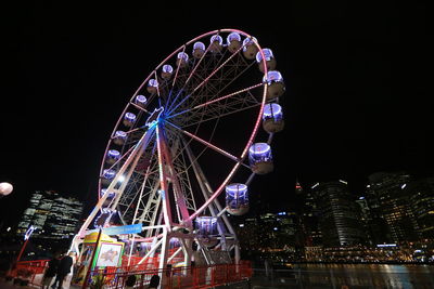 Low angle view of illuminated ferris wheel against buildings at night