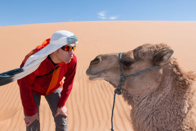 Tourist with turban and sunglasses kissing a camel in the desert dunes